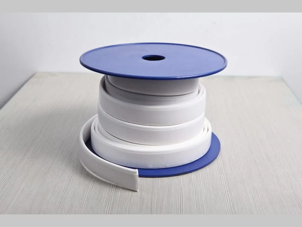 Băng PTFE giãn nở: Băng PTFE trắng bản rộng cuộn trên lõi, đầu băng thả xuống mặt bàn