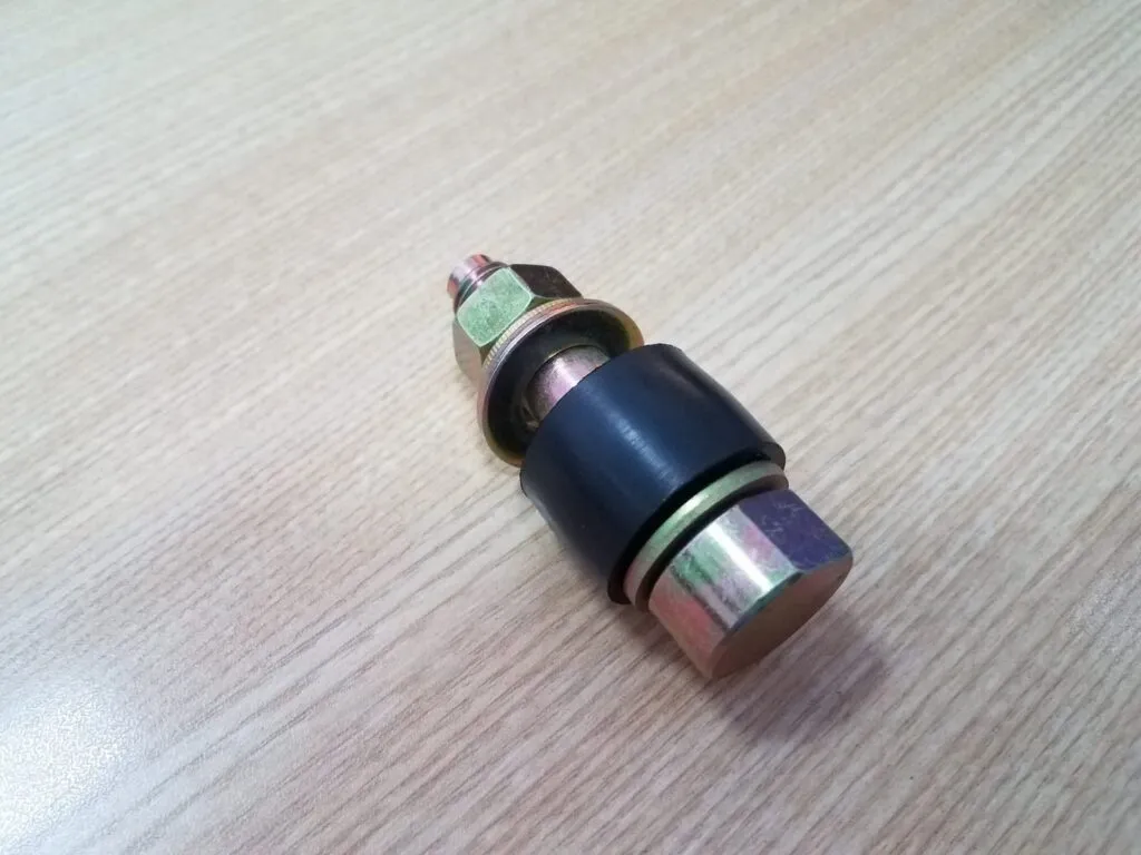 Cao su khớp nối chốt: Một chốt thép lắp ống cao su đen và đai ốc đứng trên bàn