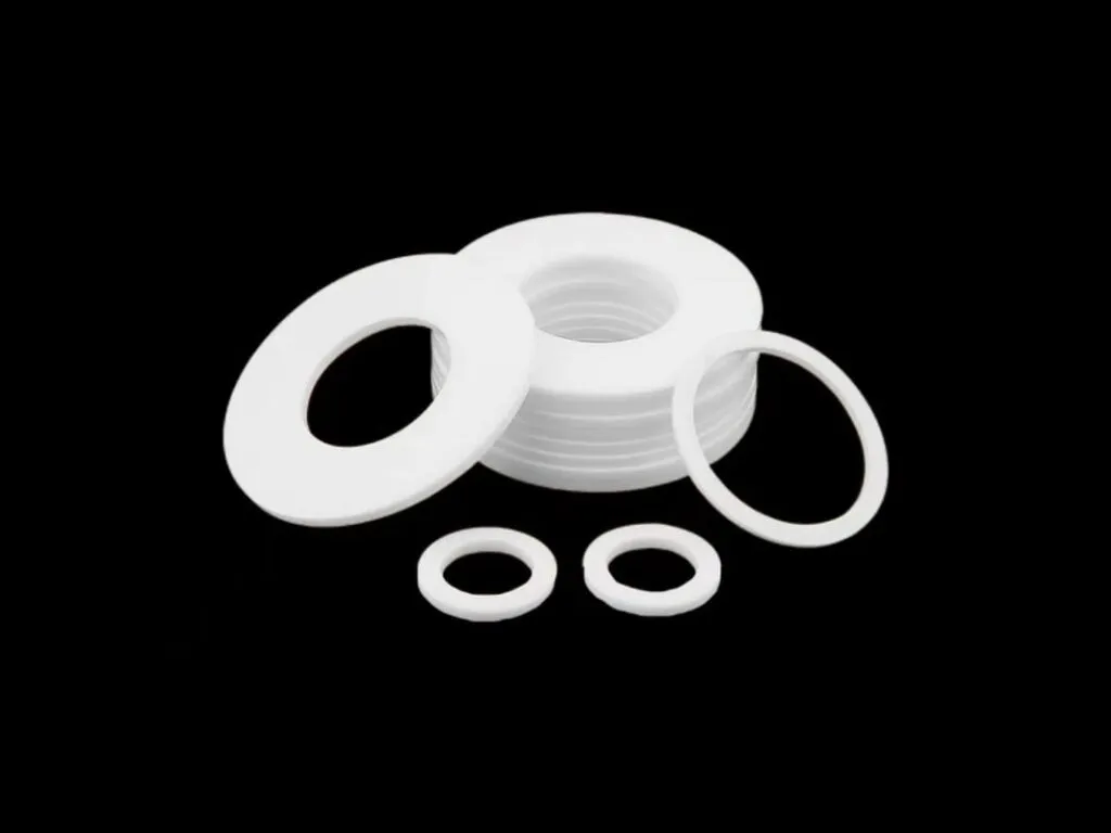 Gioăng PTFE mặt bích: Gioăng PTFE trắng cỡ lớn cùng vòng nhỏ xếp lẫn trên nền đen