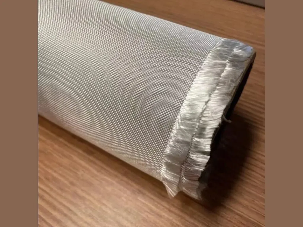 Vải thủy tinh chịu nhiệt: Cuộn vải thủy tinh xám sợi bung ở mép trên mặt gỗ