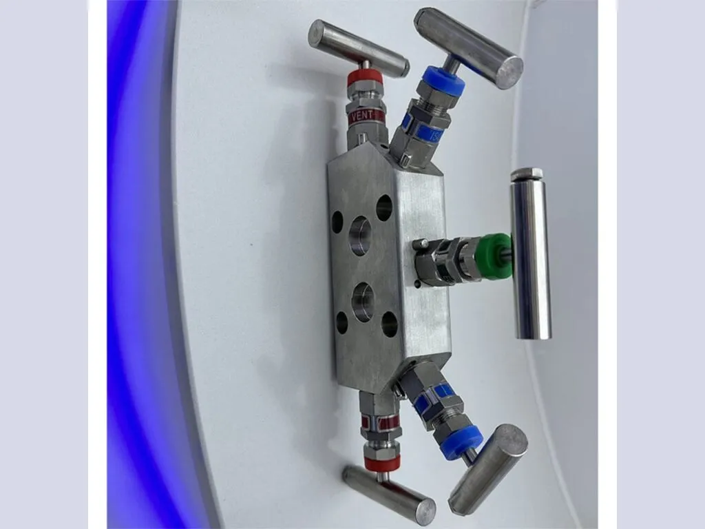 Van kim đồng hồ áp suất: Cụm van kim năm van inox chụp từ trên xuống trên nền xám